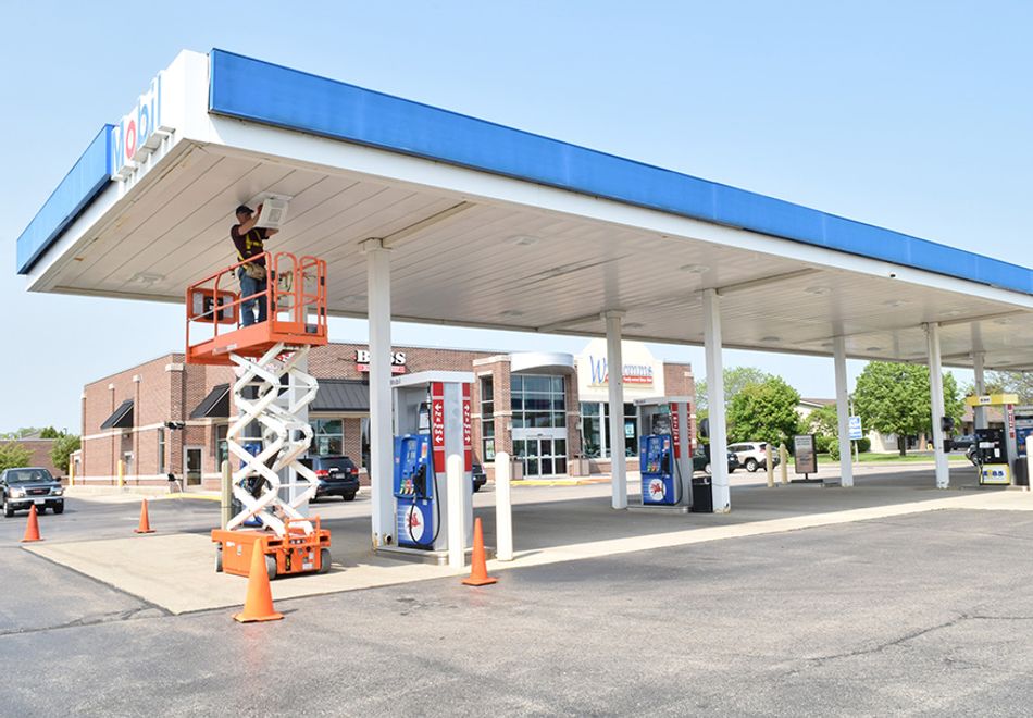 man in a scissor lift at a gas station installing lighting in the canopy covering gas pumps